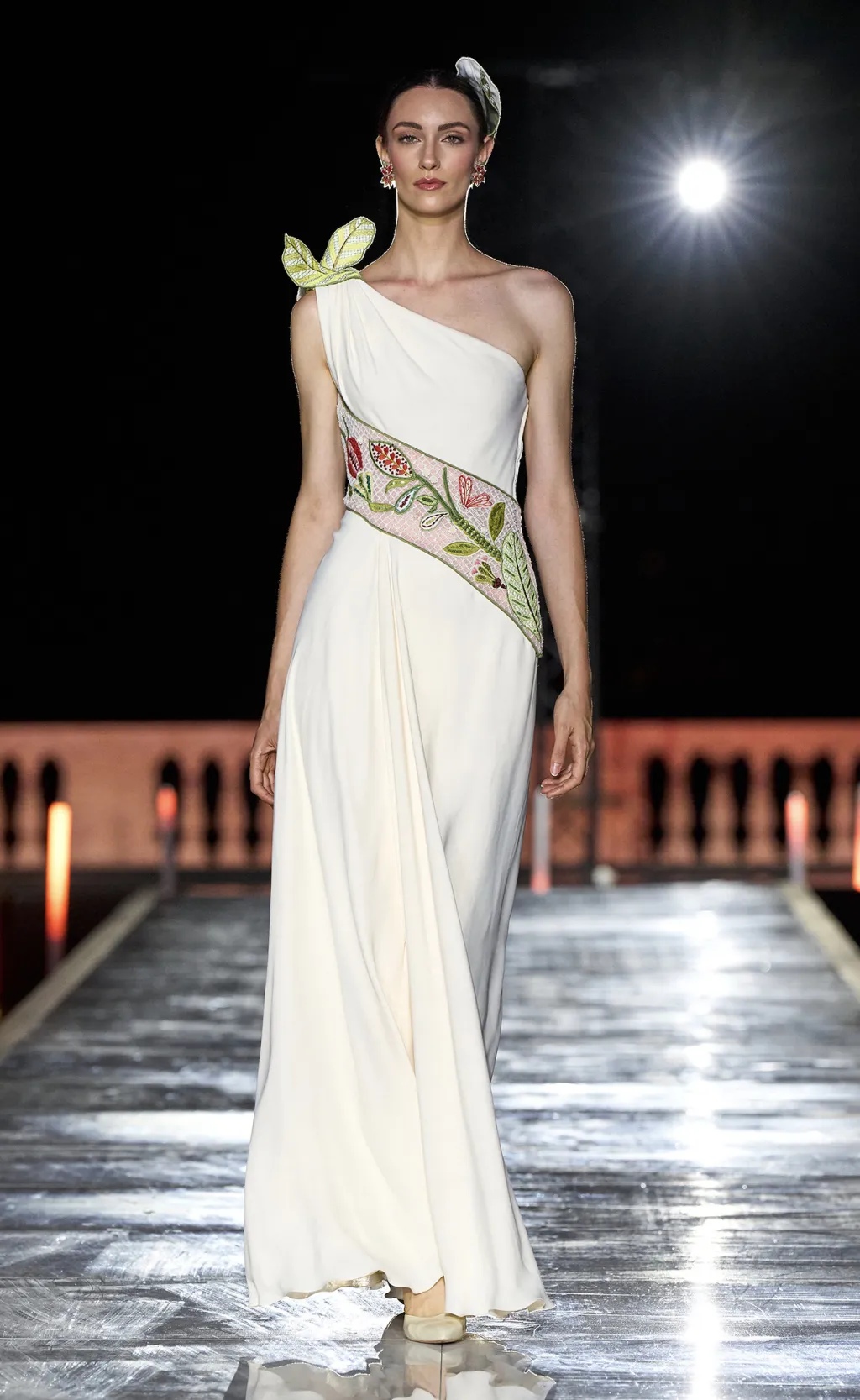 Ivory one-shoulder gown with an embroidered floral sash on the runway